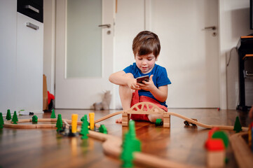 A young child deeply focused on playing with a wooden train set, constructing his own little world...