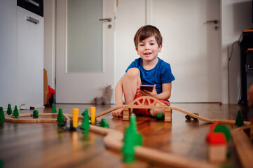 A young child deeply focused on playing with a wooden train set, constructing his own little world on the living room floor, showcasing early learning and creativity