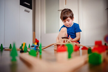 A young boy sits thoughtfully among colorful wooden toys, holding a smartphone, representing the intersection of traditional play and modern technology