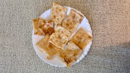Fried pancakes-envelopes with cottage cheese, in form of envelopes in pita bread on white plate on table against background of a tablecloth