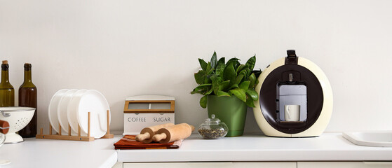 Modern coffee machine, houseplant and utensils on white kitchen counter