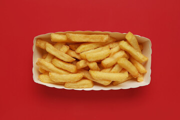 Paper box with tasty french fries on red background