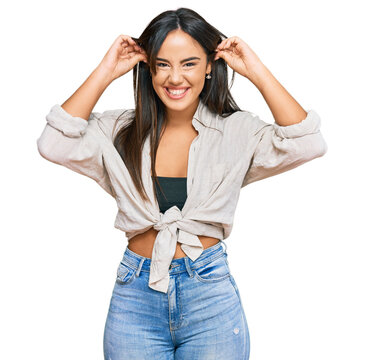 Young beautiful hispanic girl wearing casual clothes smiling pulling ears with fingers, funny gesture. audition problem