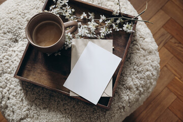 Spring still life composition. Greeting card mockup, cup of coffee. Feminine photo. Floral scene. Blurred cherry tree blossoms on wool taburet, stool. Defocused wooden parquet floor. Top view.