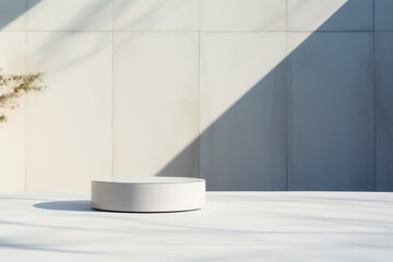 White cylinder on white table made of composite material. Empty courtyard, outdoor concrete product podium with stark shadows in midday sun