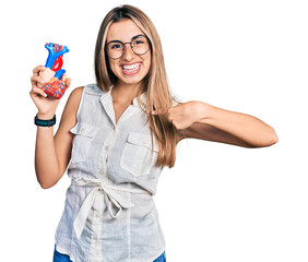 Hispanic young woman holding heart organ pointing finger to one self smiling happy and proud
