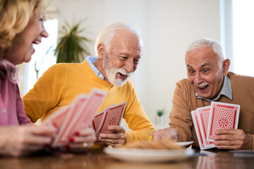 Group of happy mature friends having fun while playing cards at home.