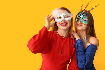 Happy young women in carnival masks on yellow background