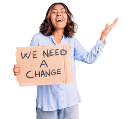 Young beautiful mixed race woman holding we need a change banner celebrating victory with happy smile and winner expression with raised hands