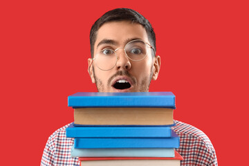 Young man with stack of books on red background