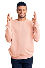 Fototapeta premium Young hispanic man wearing casual clothes gesturing finger crossed smiling with hope and eyes closed. luck and superstitious concept.