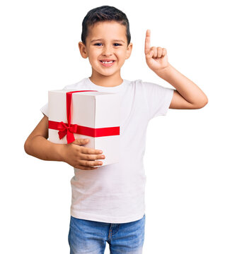 Little cute boy kid holding gift surprised with an idea or question pointing finger with happy face, number one