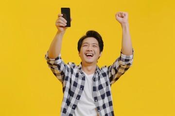 Happy asia male holding smartphone and arm up with successful achievement isolated yellow background