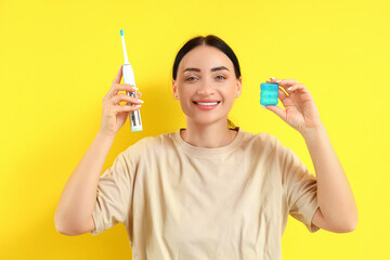 Beautiful young happy woman with dental floss and electric toothbrush on yellow background