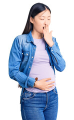 Young beautiful chinese woman pregnant expecting baby bored yawning tired covering mouth with hand. restless and sleepiness.