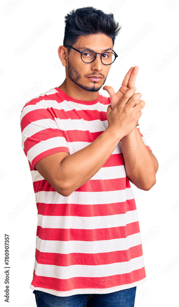 Sticker Handsome latin american young man wearing casual clothes and glasses holding symbolic gun with hand gesture, playing killing shooting weapons, angry face