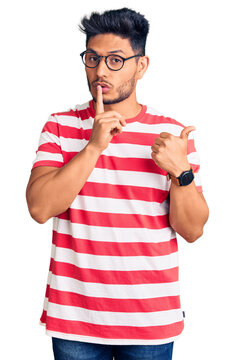 Handsome latin american young man wearing casual clothes and glasses asking to be quiet with finger on lips pointing with hand to the side. silence and secret concept.
