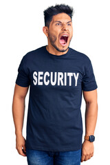 Handsome latin american young man wearing security t shirt angry and mad screaming frustrated and furious, shouting with anger. rage and aggressive concept.