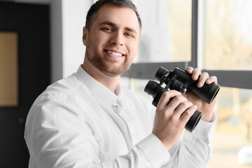 Young male businessman with binoculars near window, closeup
