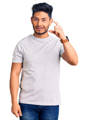 Fototapeta premium Handsome latin american young man wearing casual tshirt smiling and confident gesturing with hand doing small size sign with fingers looking and the camera. measure concept.