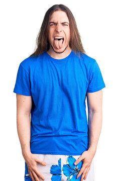 Young adult man with long hair wearing swimwear sticking tongue out happy with funny expression. emotion concept.