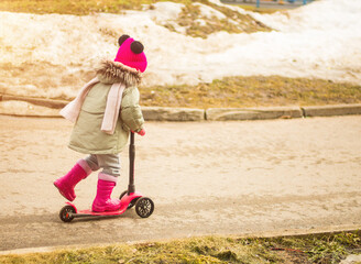 child rides a pink scooter on a spring day