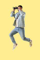 Jumping young man with binoculars on yellow background
