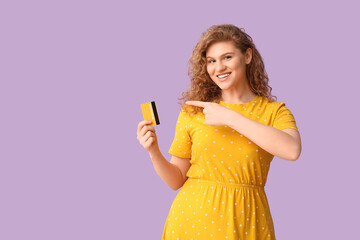 Beautiful young woman pointing at credit card on purple background