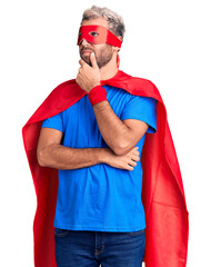 Young blond man wearing super hero custome with hand on chin thinking about question, pensive...