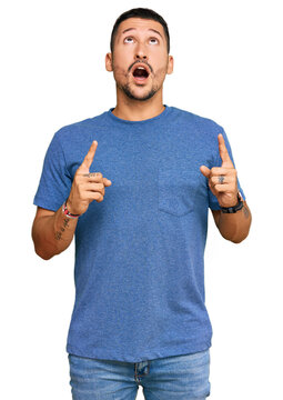 Handsome man with tattoos wearing casual clothes amazed and surprised looking up and pointing with fingers and raised arms.
