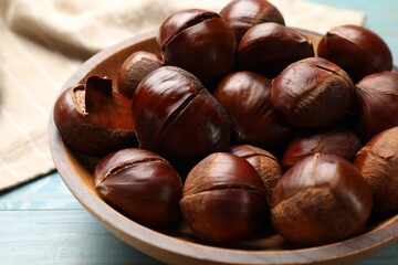 Fresh edible sweet chestnuts in bowl on light blue wooden table, closeup