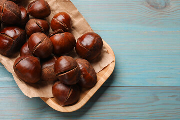 Fresh edible sweet chestnuts in serving plate on light blue wooden table, top view. Space for text