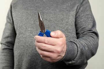 Man with needle nose pliers on light background, closeup