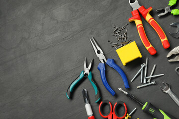 Different pliers, screwdriver, wrenches and other repair tools on black textured table, flat lay....