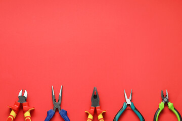 Different pliers on red background, flat lay. Space for text