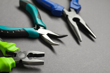 Different pliers on grey background, closeup view