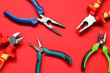 Different pliers on red background, flat lay - obrazy, fototapety, plakaty