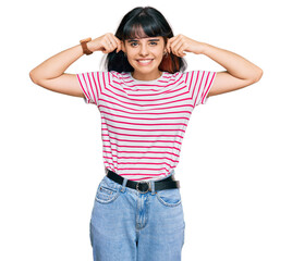 Young hispanic girl wearing casual clothes smiling pulling ears with fingers, funny gesture....