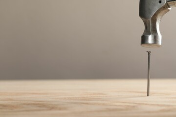 Hammering metal nail on wooden table against grey background, closeup. Space for text