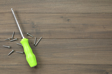 Screwdriver with green handle and screws on wooden table, flat lay. Space for text