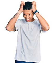 Fototapeta premium Young hispanic man wearing casual white t shirt suffering from headache desperate and stressed because pain and migraine. hands on head.