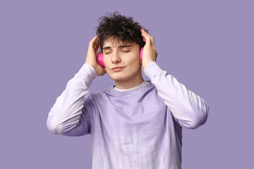 Handsome young man in stylish sweatshirt and headphones on purple background