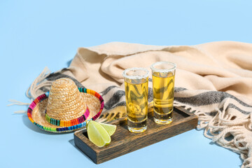 Shots of tequila and sombrero hat on blue background