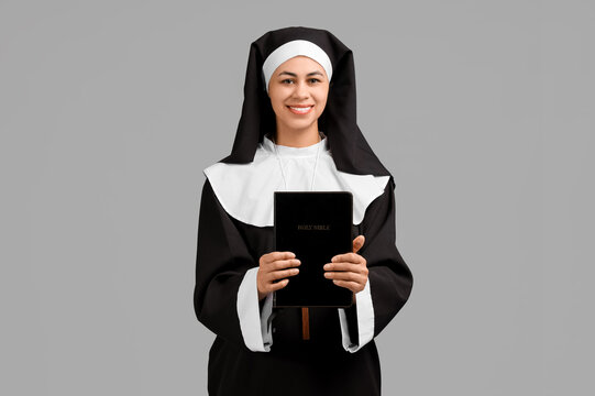 Portrait of young nun with Bible on grey background