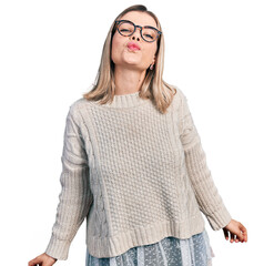 Young blonde woman wearing glasses looking at the camera blowing a kiss on air being lovely and sexy. love expression.