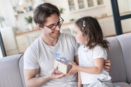 Close up image of a caring cute little kid small daughter giving her daddy a present to congratulate with father`s day, birthday. I love you, dad! Family holiday, parenthood, fatherhood