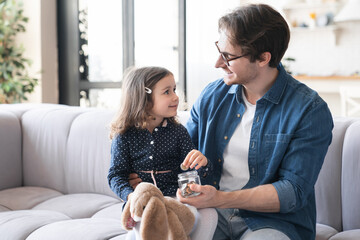 Small girl daughter and her young father putting money to the moneybox piggy bank. Personal Savings. Saving money concept. For future, mortgage loan savings home in crisis coronavirus concept.