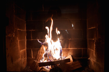 Cozy wood fire burning in brick fireplace with visible soot and heat exposure. Lively orange and...