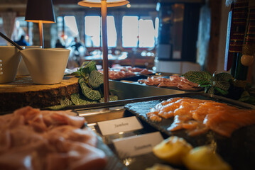 Buffet spread with smoked salmon on slate platter, labeled Salmon, rustic setting with ham slices,...