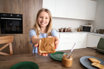 Little girl making toast with peanut butter in kitchen